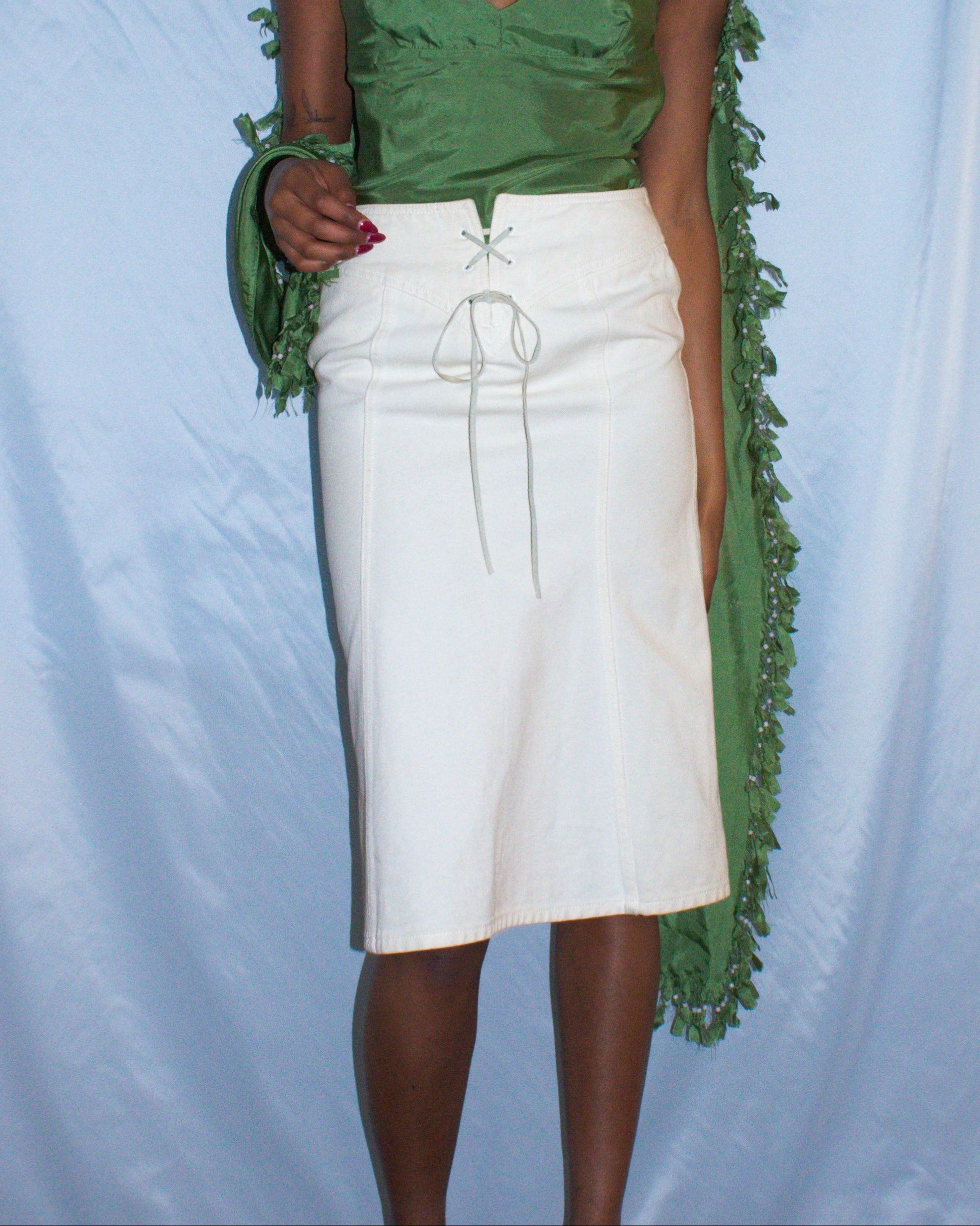 Woman wearing a green top and white skirt against a light blue backdrop